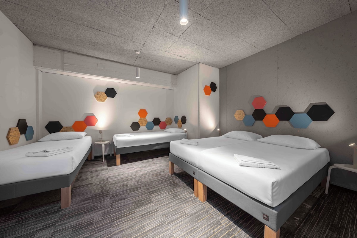 Ein Hotelzimmer mit drei Betten, einem kleinen Tisch und einer Wand mit sechsecklichen Verzierungen.