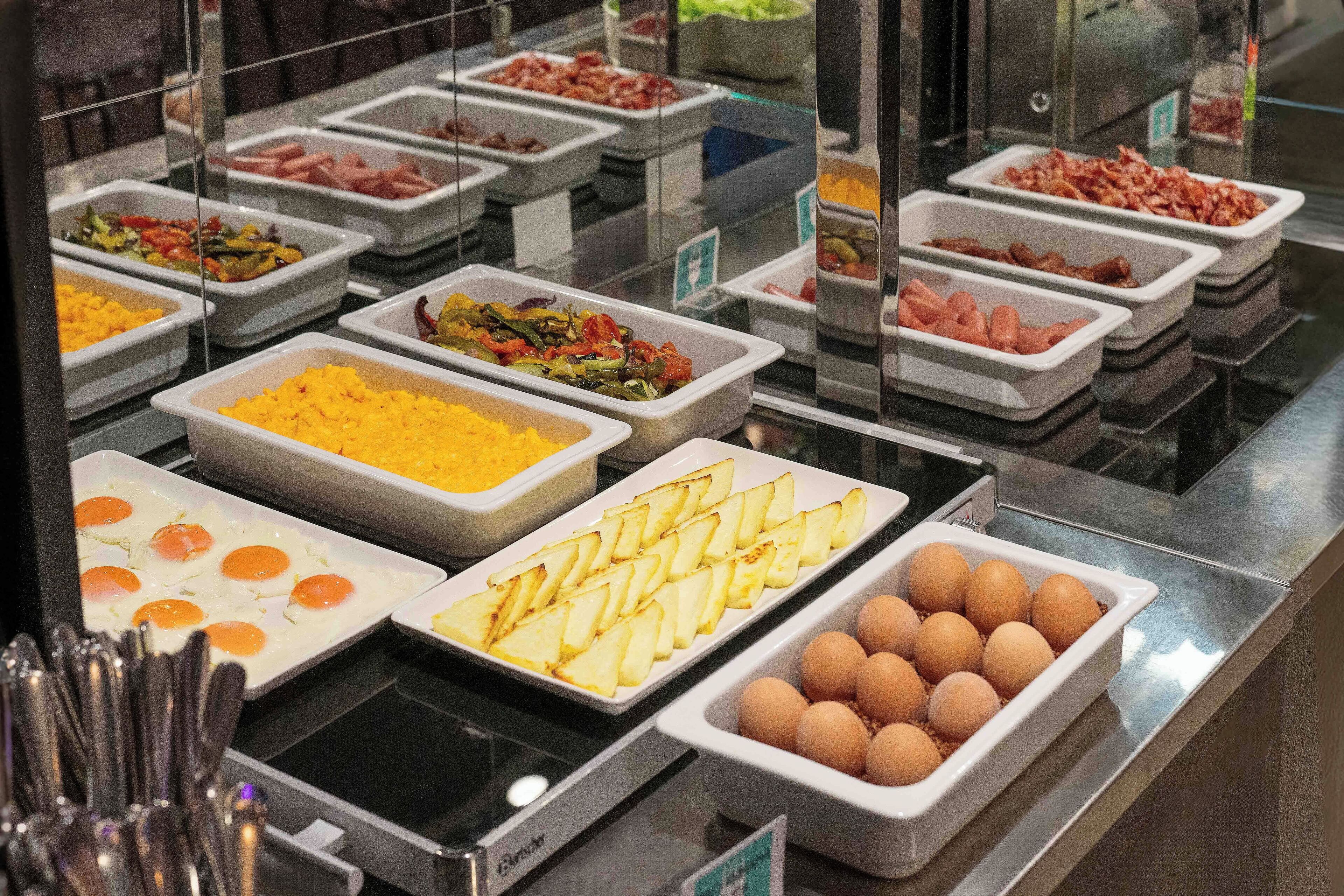 Un buffet proposant une variété de plats, notamment des œufs, des pommes de terre et différentes sortes de viande.