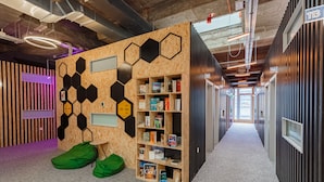 Un interior moderno con una pared hexagonal de madera, una estantería y sillones orejeros verdes.