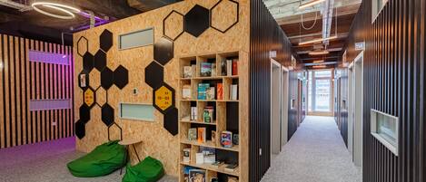 Un interior moderno con una pared hexagonal de madera, una estantería y sillones orejeros verdes.