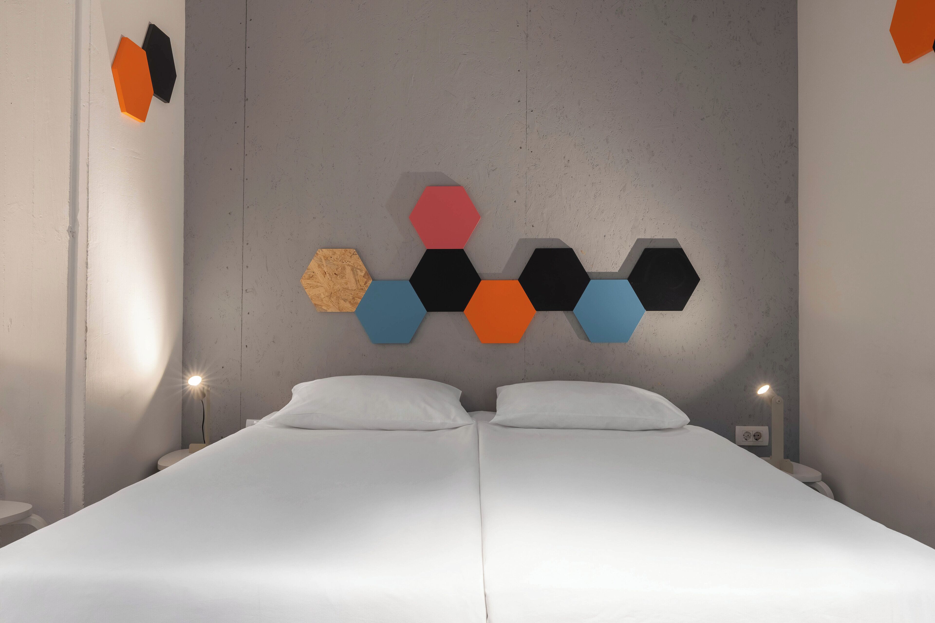 Ein Doppelbett mit weißen Leinen, eine graue Strukturwand und ein sechseckiges Wandkunstwerk.