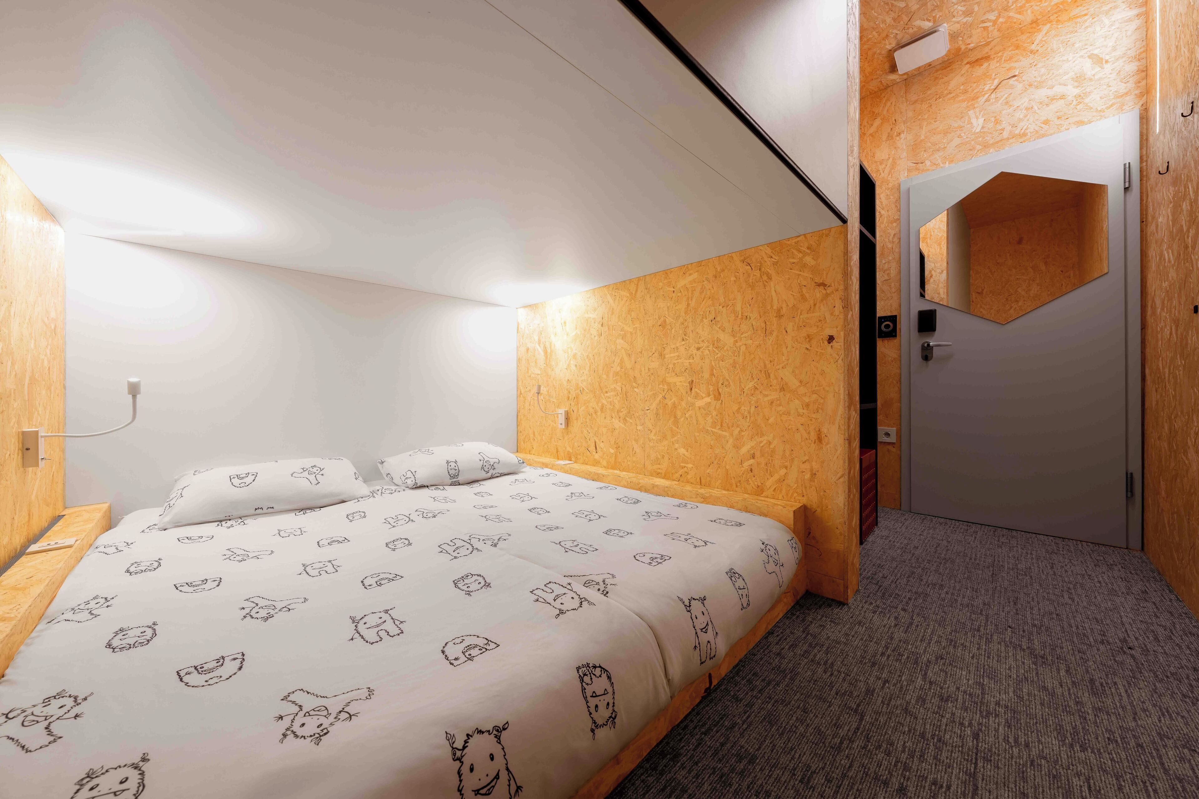 Ein Schlafzimmer mit einem Bett, einem Holz-Kopfteil, einer Tür mit Spiegel und einem Teppichboden.