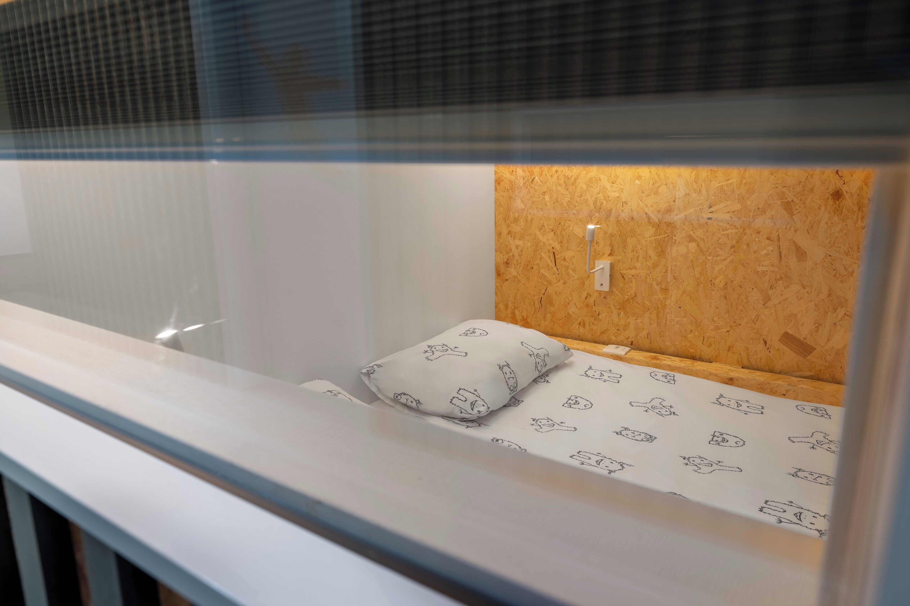 A bunk bed with a wooden headboard, a white mattress with a pattern, and a pillow with a similar design.