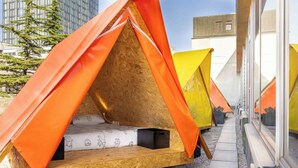 Una hilera de tiendas modernas, triangulares, con base de madera y paredes de tela naranja y amarilla, alineadas frente a un edificio con grandes ventanales.