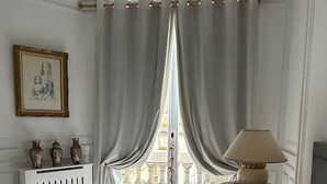 Une chambre à coucher avec un grand lit, une table de chevet avec une lampe, une fenêtre avec des rideaux et un radiateur.