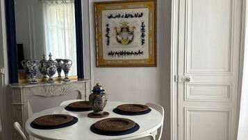 Zona pranzo con tavolo bianco, quattro sedie, uno specchio decorativo, un'opera d'arte incorniciata e una porta bianca.