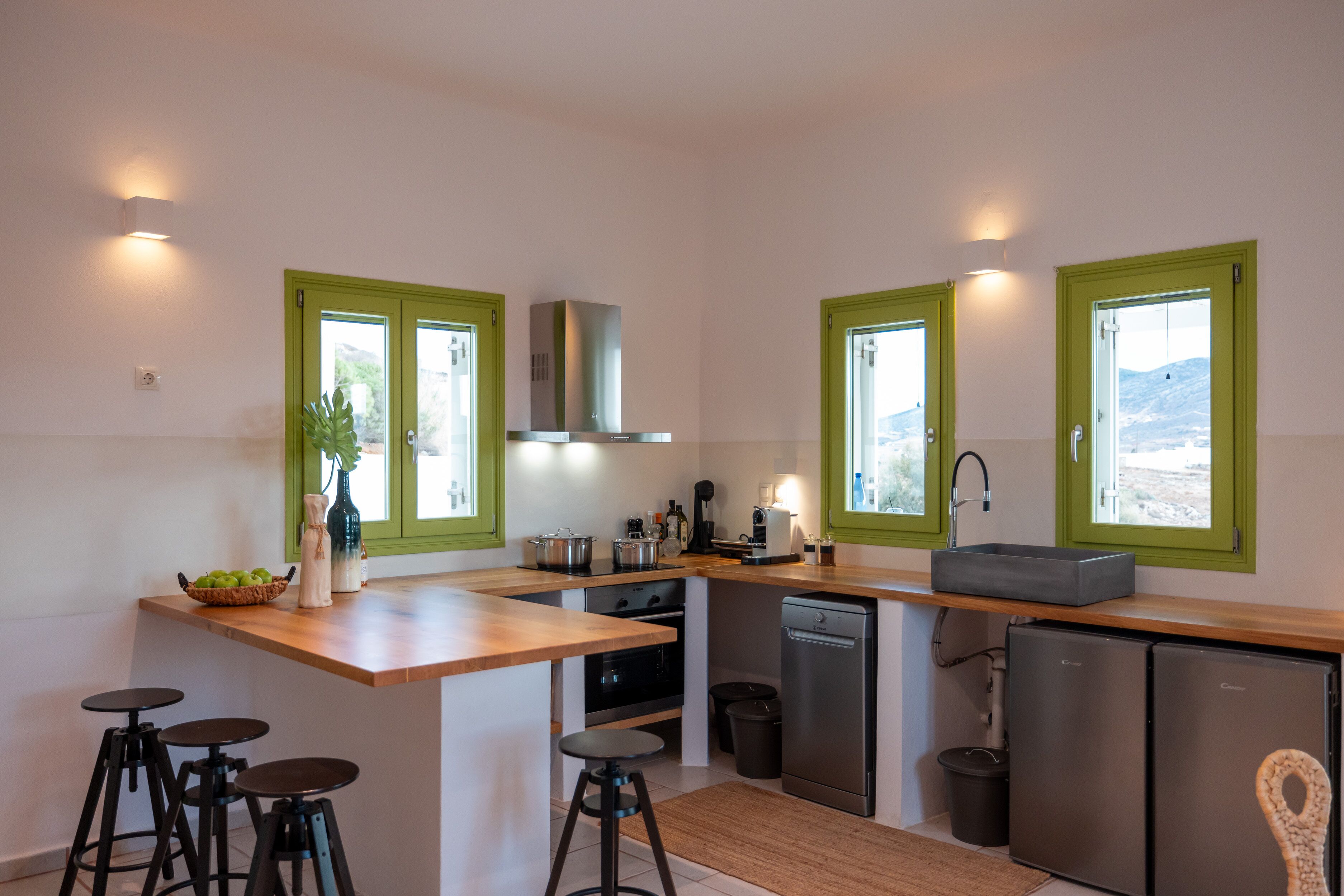 A modern kitchen with green-framed windows, a central island with stools, and built-in appliances.