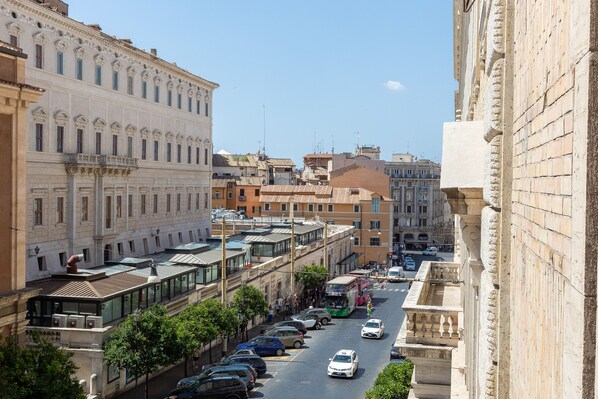 A street view with historic buildings, parked cars, and a clear sky.
