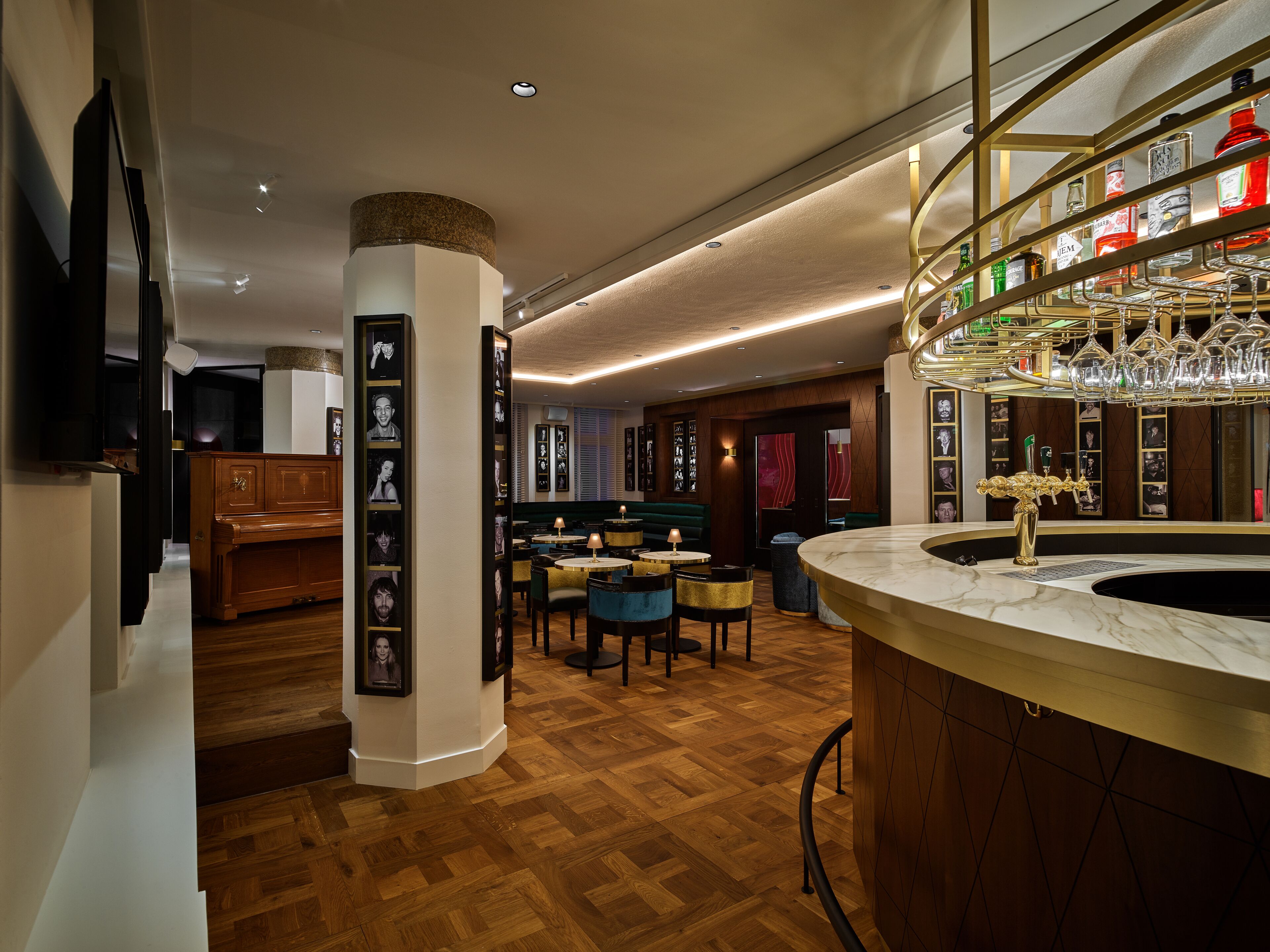 A modern bar area with a marble counter, wooden flooring, and a variety of liquor bottles.