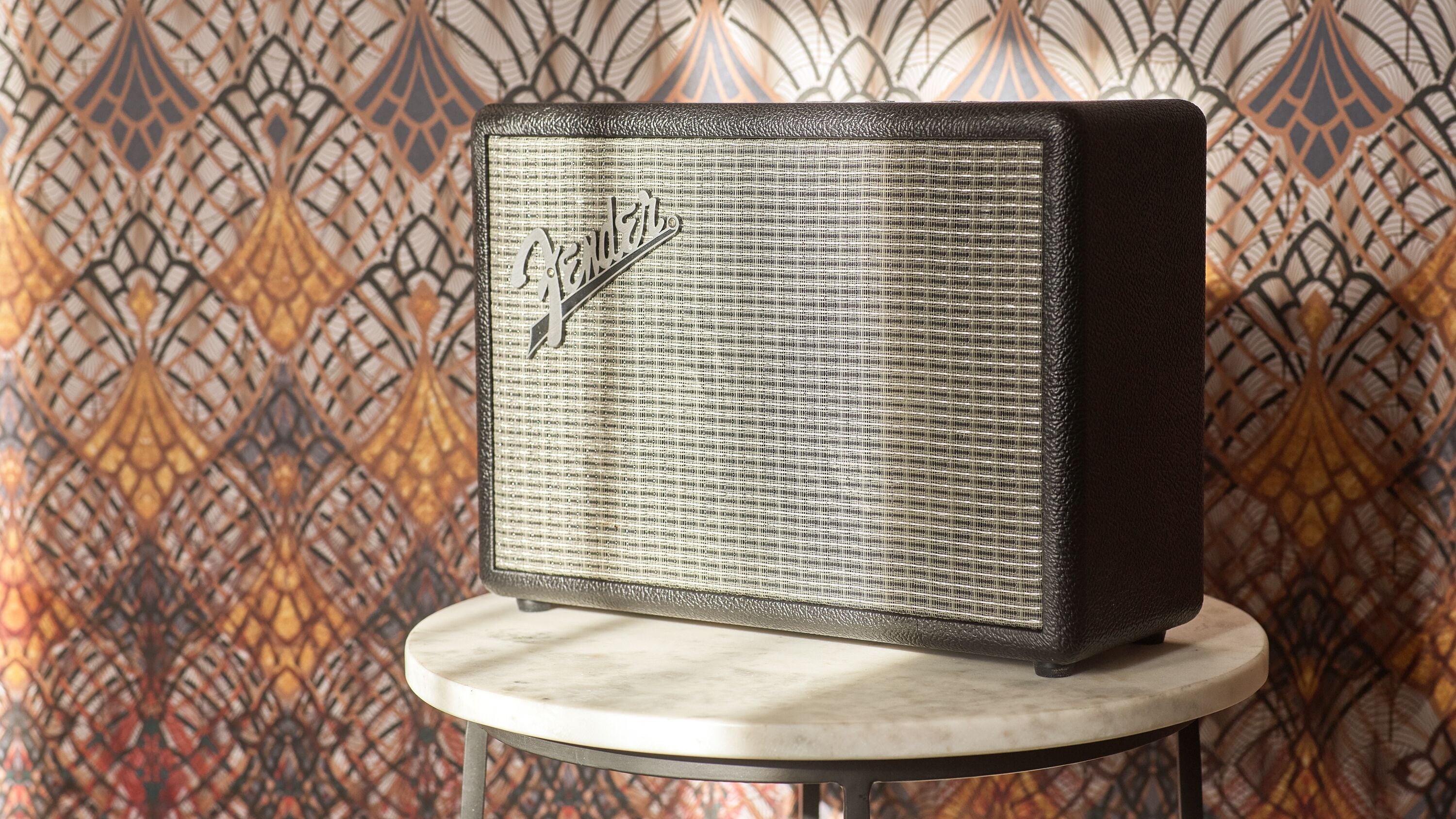A vintage-style speaker on a small round table against a patterned wallpaper background.