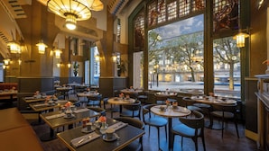 Ein Restaurant mit mehreren Tischen und Stühlen, großen Fenstern mit Blick auf die Straße und dekorativer Beleuchtung.