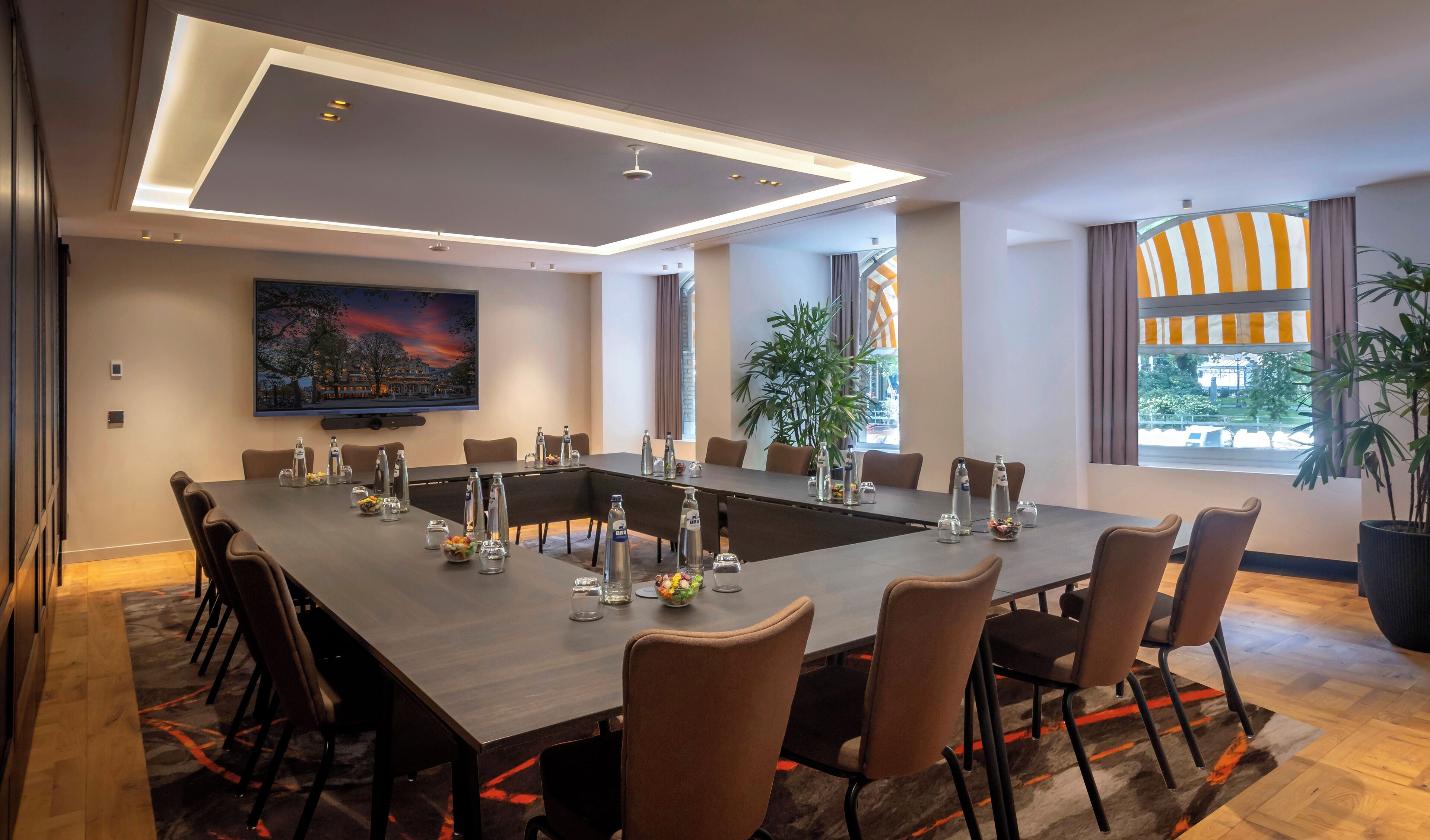 Ein moderner Konferenzraum mit einem langen Tisch, Stühlen und einer großen Leinwand.