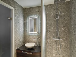 Une salle de bain avec un mur en granit, un lavabo blanc, un miroir et une douche.
