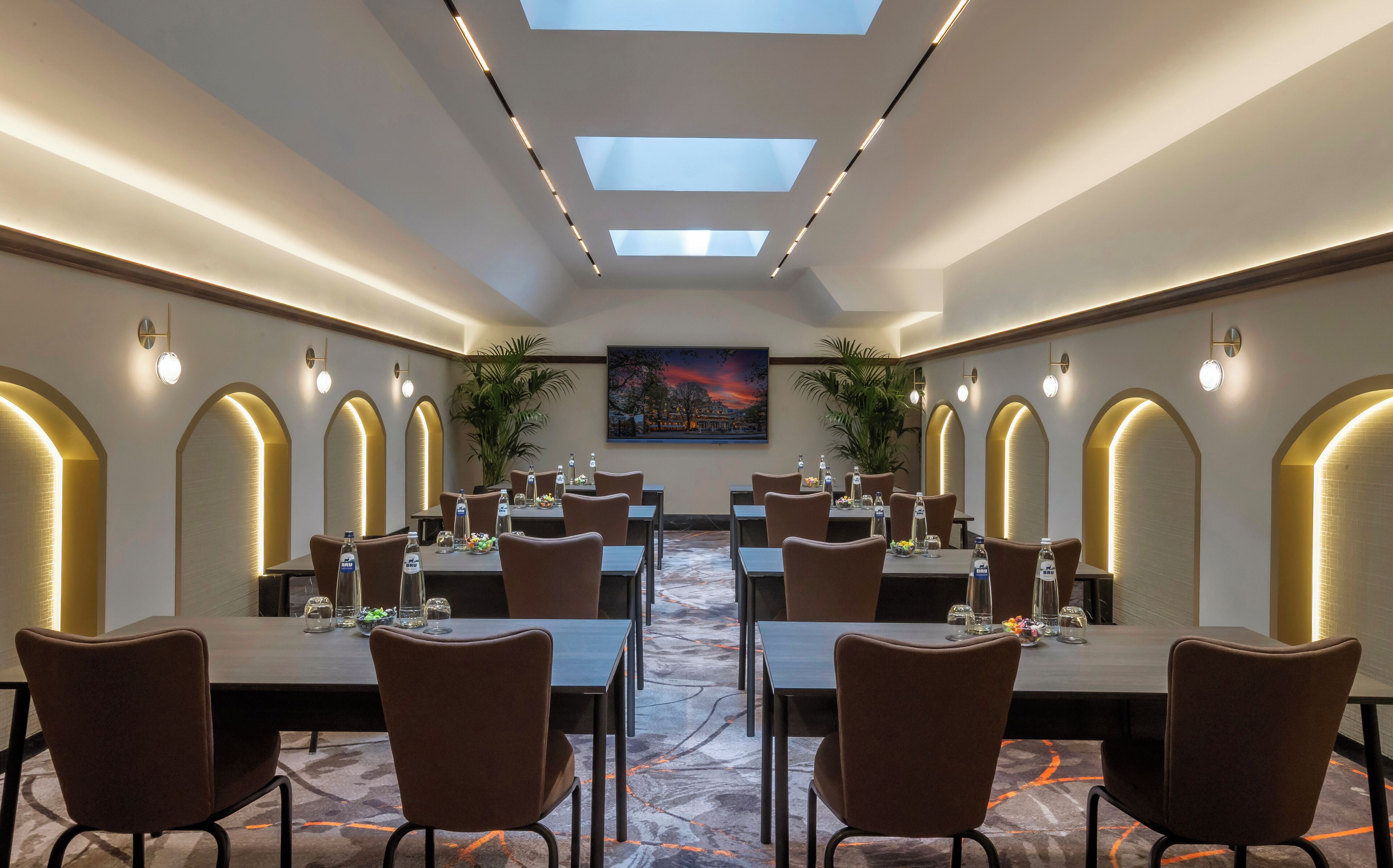 A conference room with tables and chairs, skylights, and a large painting on the wall.