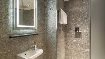 Un baño moderno con pared de ducha de granito, un lavabo blanco y un espejo con marco iluminado.