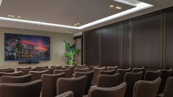 Een vergaderzaal met rijen stoelen, een groot schilderij van een zonsondergang en een plant.