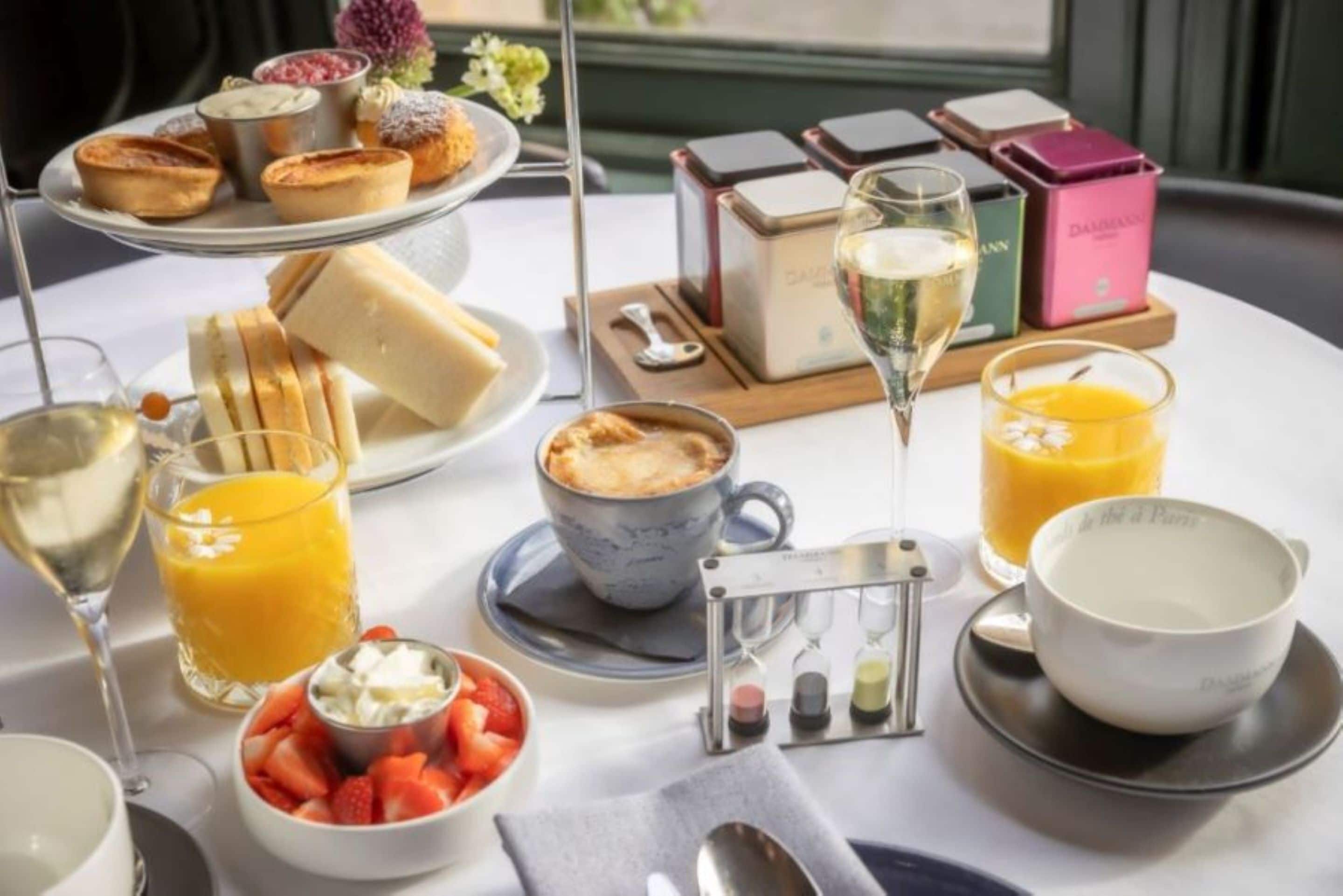 A breakfast setting with pastries, fruit, juice, and a coffee cup on a table.