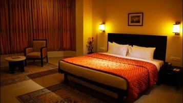A hotel room with a large bed, two bedside tables, a chair, a carpeted floor, and curtains.