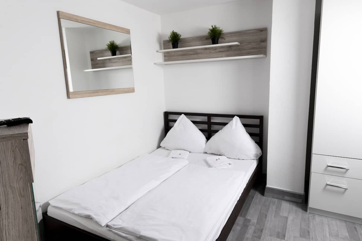A neatly arranged bedroom with a bed, a bedside table, a mirror, and built-in shelves with plants.