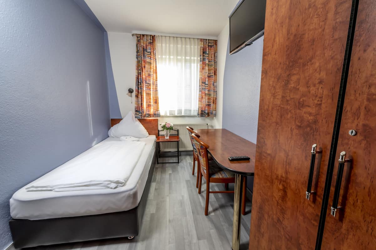 A compact room with a single bed, a small table, and a chair.