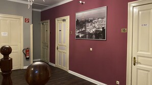 A hallway with a chandelier, numbered doors, and a cityscape painting. - Quickborner Hof (Quickborn)