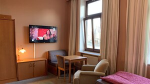 A hotel room with a bed, a desk, a chair, a television, and a window with curtains. - Quickborner Hof (Quickborn)