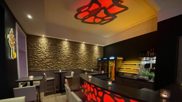 A modern bar area with a unique red-lit design, a stone-textured wall, and a bar counter with a wine display. - Quickborner Hof (Quickborn)