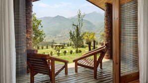 Una terraza de madera con dos sillas de madera orientadas a una vista panorámica de la montaña a través de un ventanal grande.