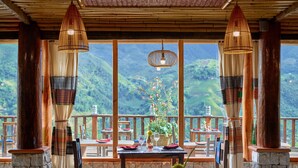 Un comedor con una mesa dispuesta para dos, ventanas amplias con vista a la montaña, y lámparas de tejido tradicional.