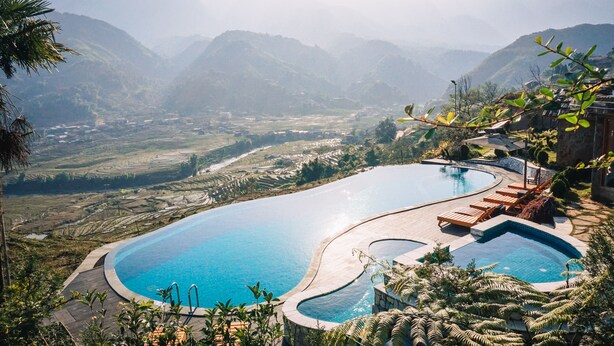Una piscina con diseño curvo, rodeada de sillas de descanso y un paisaje montañoso al fondo.