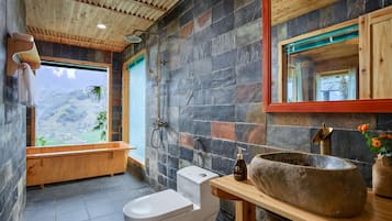 A bathroom with a stone wall, wooden ceiling, and a large window with a view of greenery.