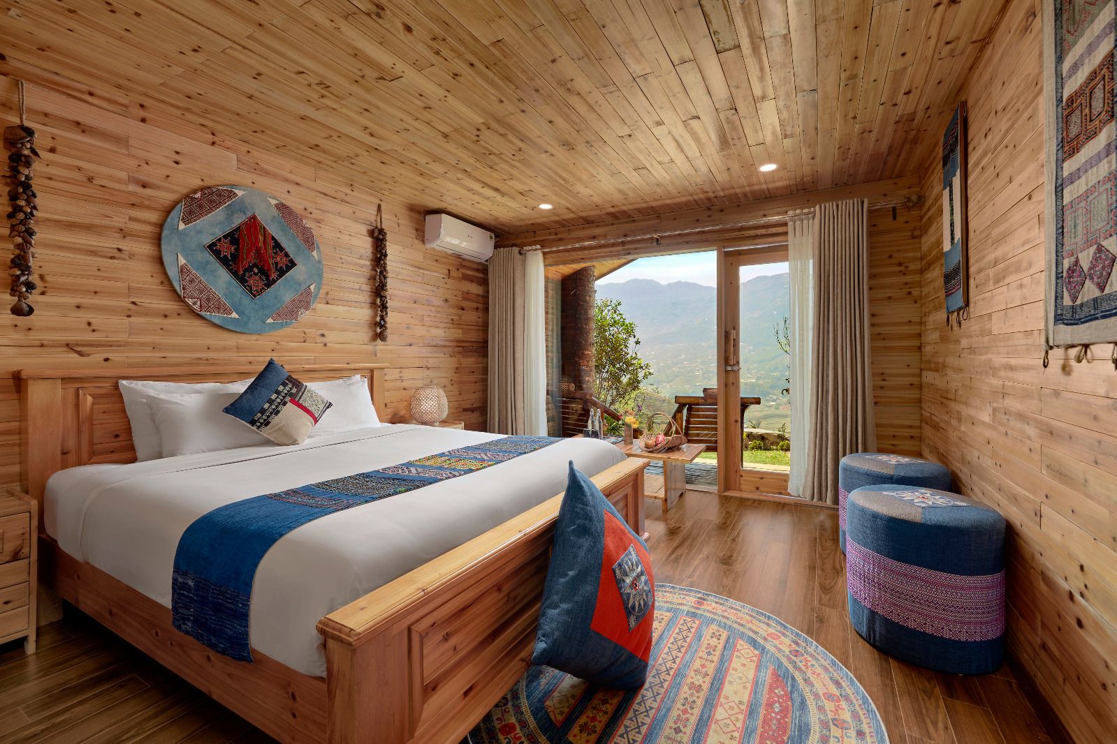 A wooden cabin bedroom with a bed, a view through a glass door, and a round rug.