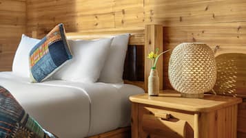 A wooden cabin interior with a bed, a nightstand, a decorative wall hanging, and a patterned throw blanket.