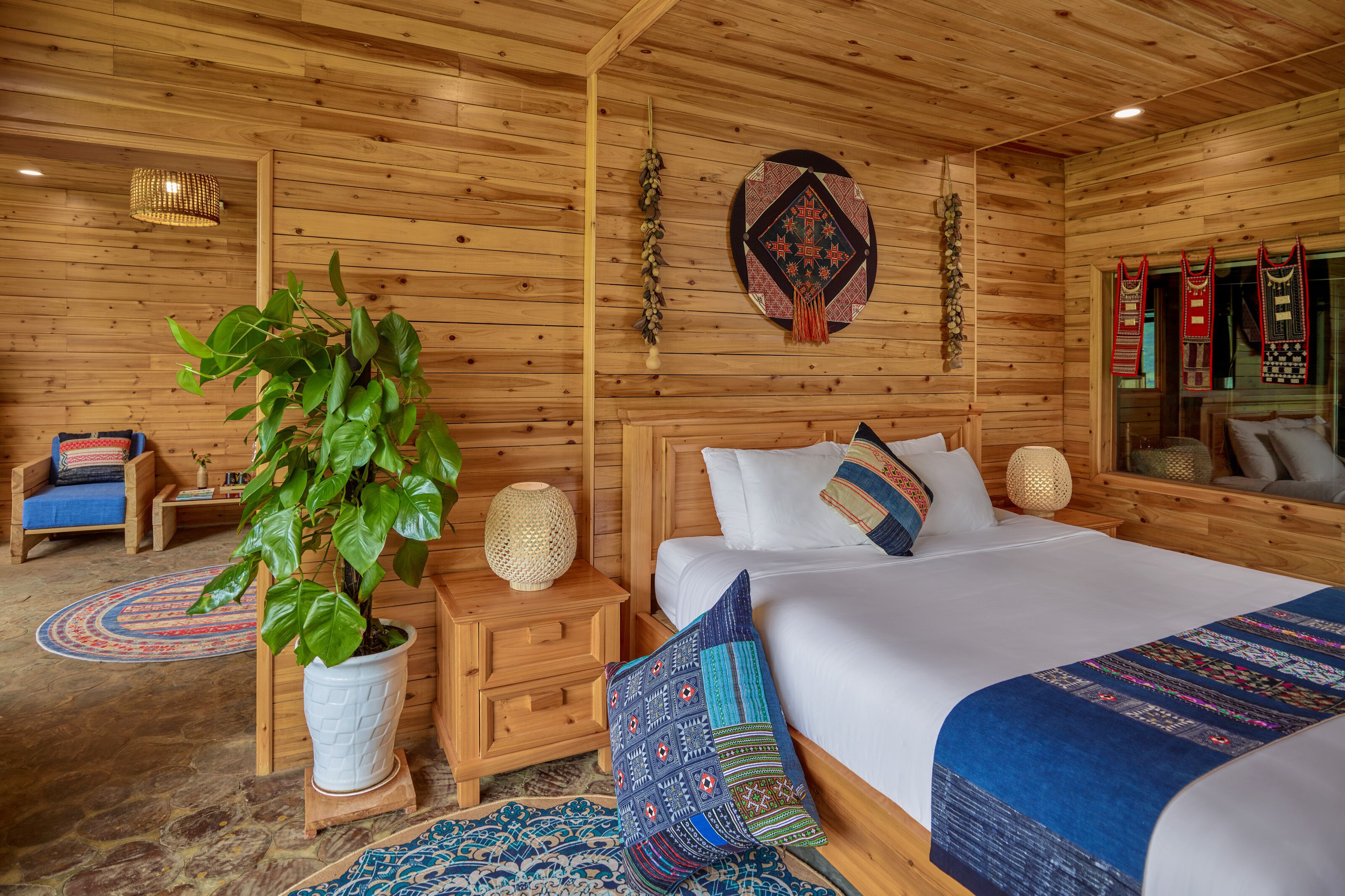 Una habitación estilo cabaña de madera con una cama grande, una mesita de noche, una planta en maceta y una alfombra tejida.