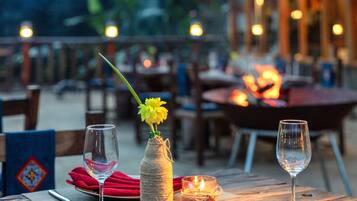 A wooden table set with a wine glass, a candle, and a vase with a yellow flower.
