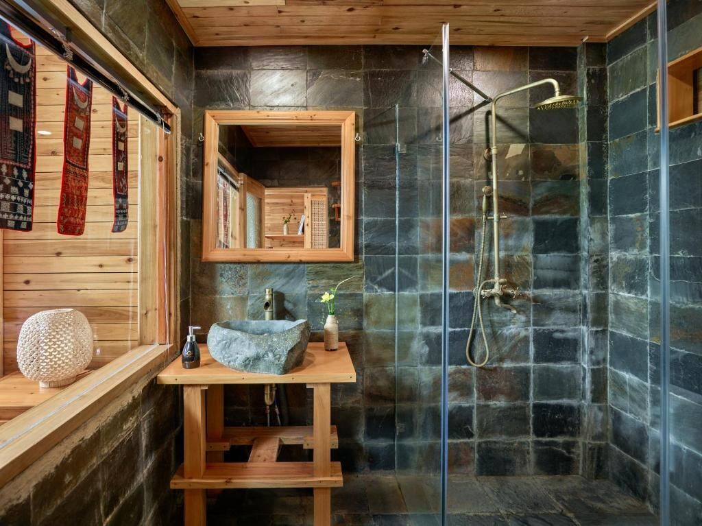Un baño de cabaña de madera con ducha de piedra, tocador de madera y espejo.