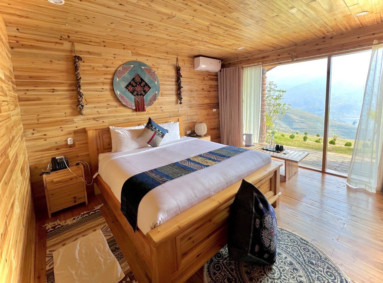 Un dormitorio de madera con una cama grande, una mesita de noche, una lámpara de noche, un reloj en la pared y vistas al exterior.
