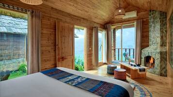 A wooden cabin bedroom with a large bed, a stone fireplace, and a view of the outdoors.