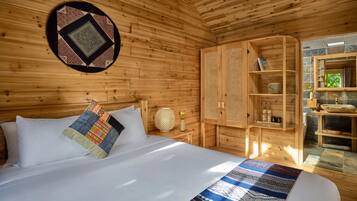 Een houten kamer met een bed, een geweven vloerkleed, een rieten mand en een plank met potten.