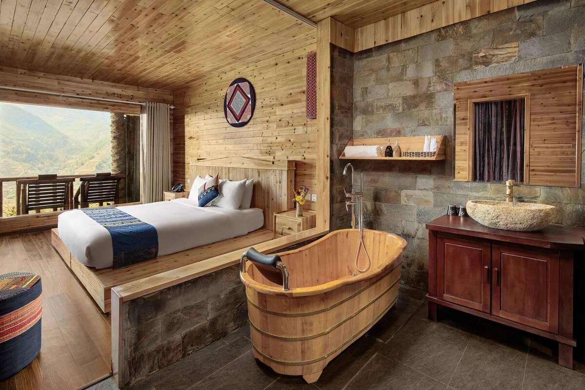 Une chambre dans une cabane en bois, avec un grand lit, une baignoire en bois et un mur en pierre.