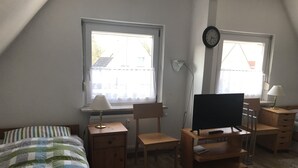 Un dormitorio con una cama, un escritorio, una silla, un televisor y dos ventanas.