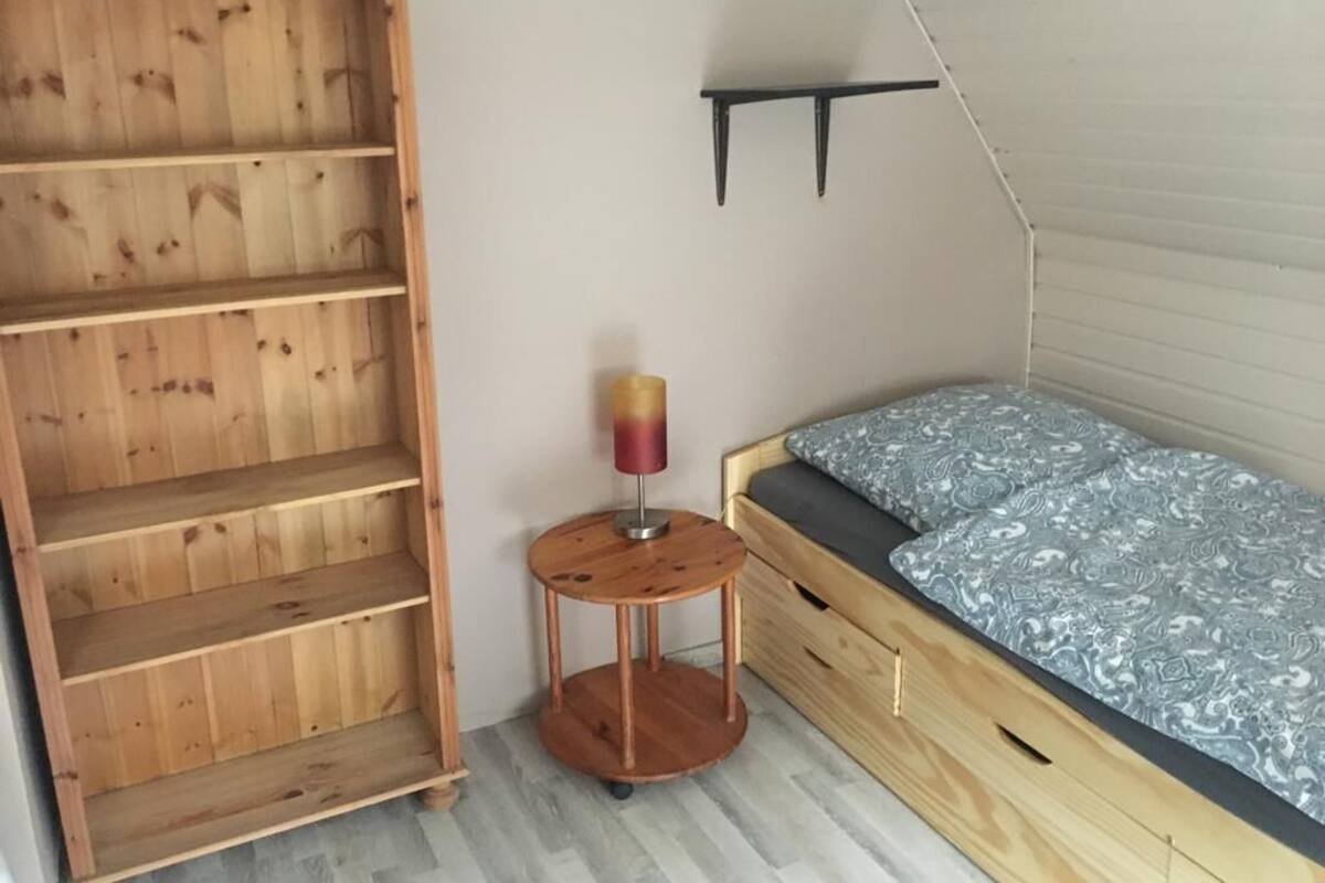 Une pièce avec une bibliothèque en bois, une petite table ronde avec une lampe, et un lit avec une literie à motifs.