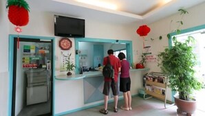 Un espace d’accueil avec un comptoir, un téléviseur fixé au-dessus et une plante en pot sur la droite.