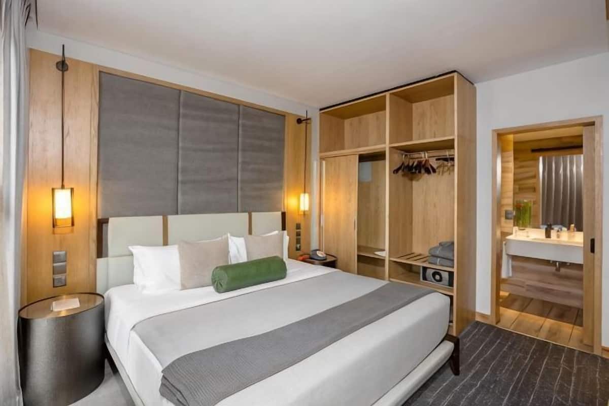 A hotel room with a large bed, bedside tables, a wardrobe, and a bathroom visible through an open door.