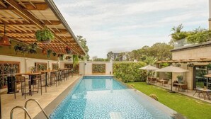 Une piscine dont le fond est recouvert de carreaux décoratifs, entourée d’un espace de détente extérieur et de verdure.