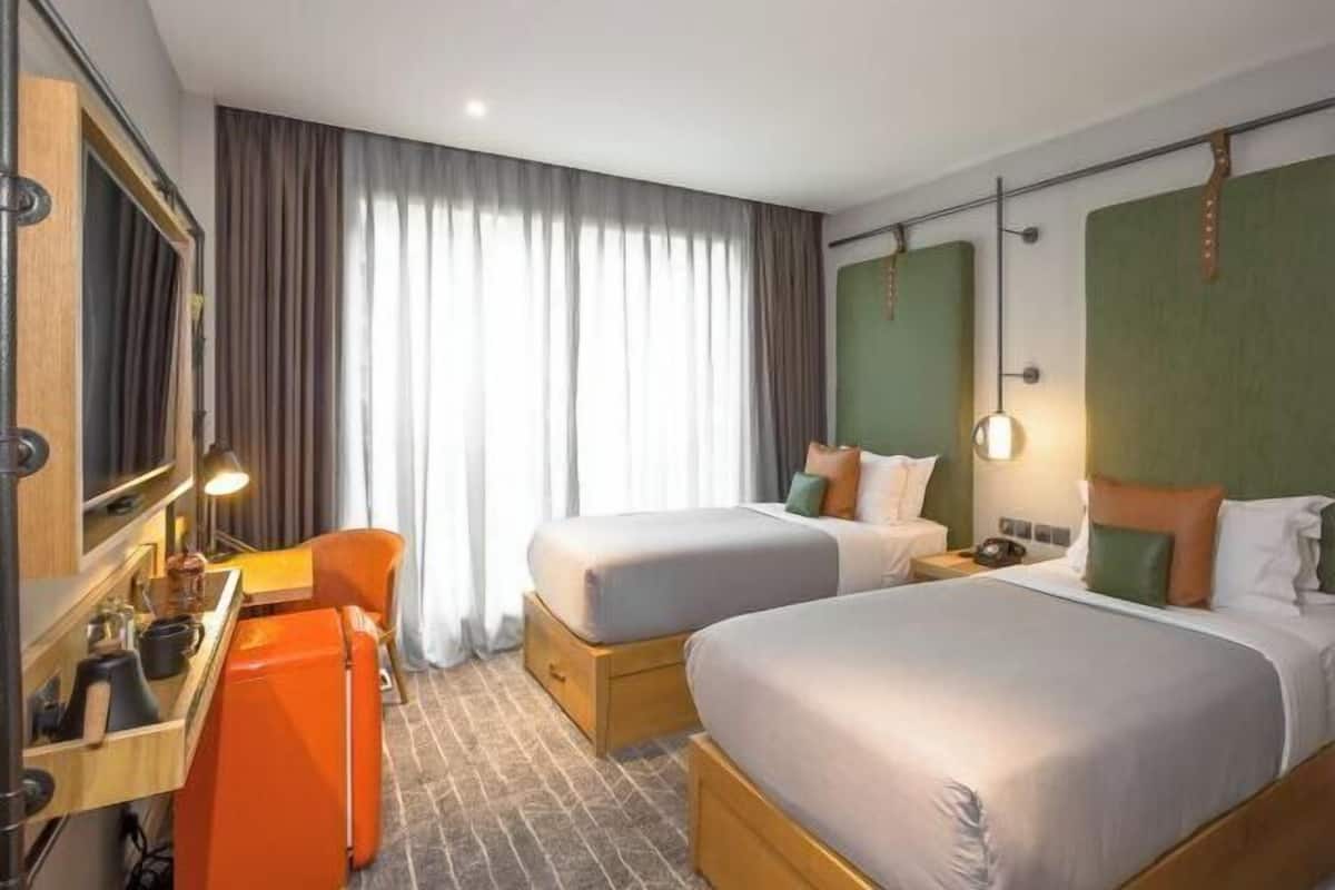 A hotel room with two beds, a desk, a chair, and a large window with curtains.