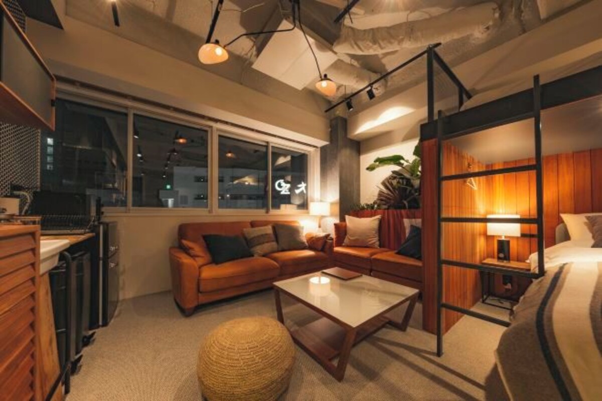 A modern hotel room with a sofa, a coffee table, and a bed. There is a window with a view of the city at night.