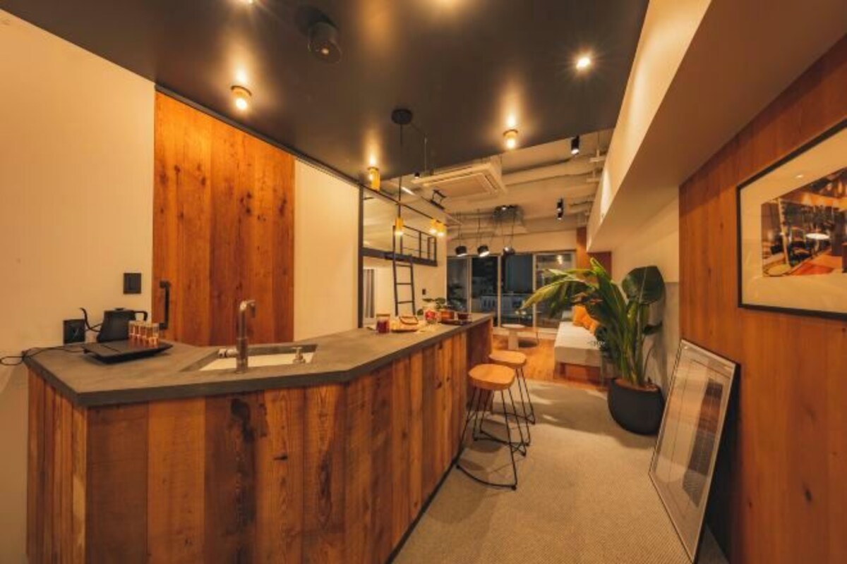 A modern kitchen with a wooden bar area, bar stools, and a large window providing natural light.