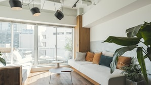 A modern living room with a white sofa, wooden floor, large windows, and a view of the city. - illi Sun Shimokitazawa (Tokyo)