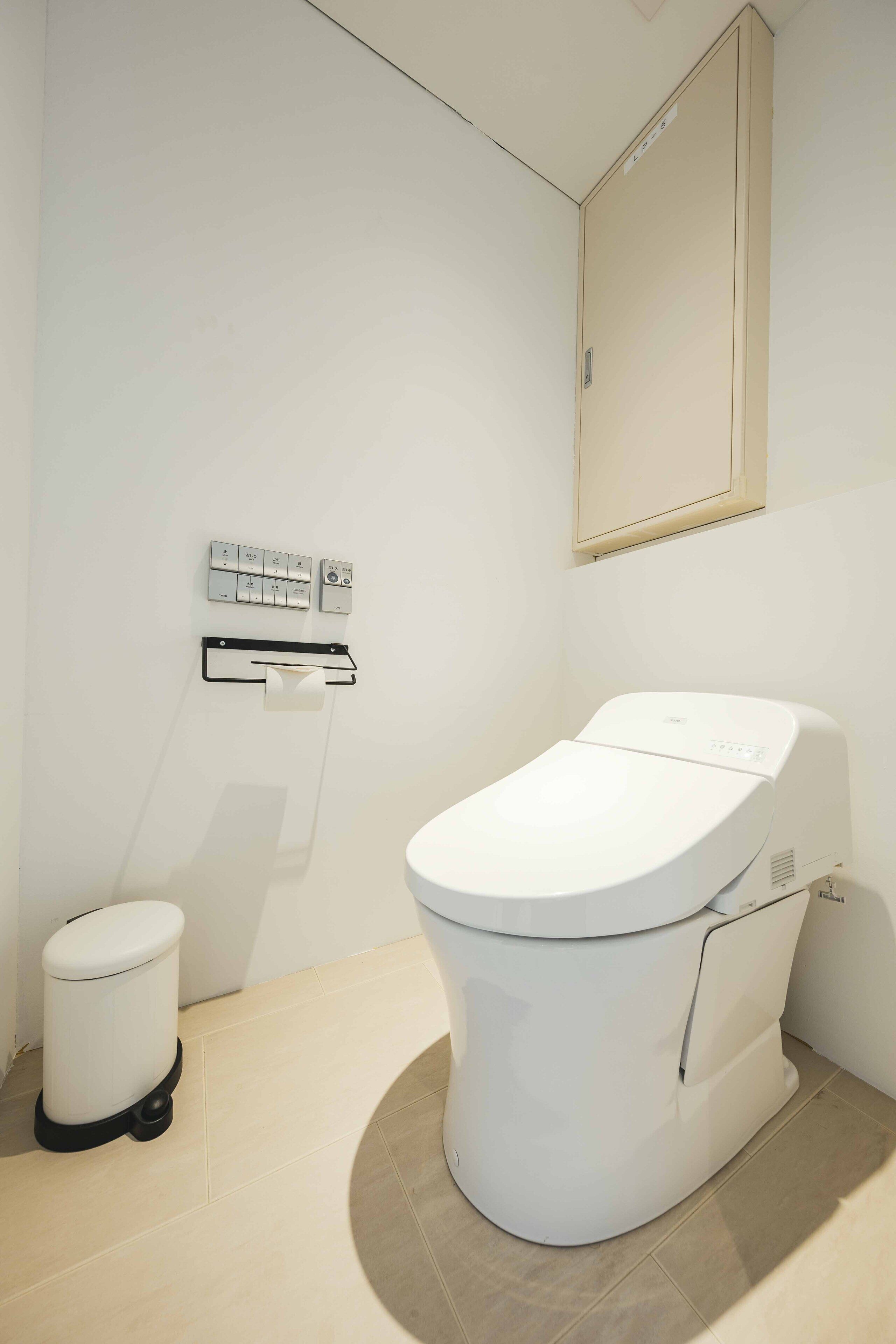 A modern bathroom with a white toilet, a trash bin, and a wall-mounted control panel.